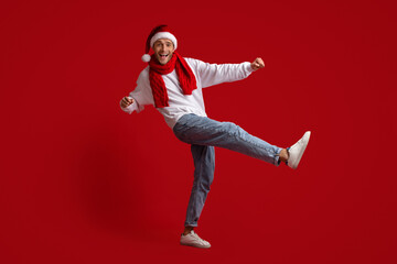 Cheerful Young Man Wearing Santa Hat And Red Scarf Dancing In Studio