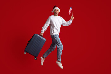 Excited Young Man In Santa Hat Jumping With American Flag And Suitcase