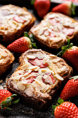 Bostock a French pastry made of sliced brioche with frangipane cream, strawberries and almond flakes, sprinkled with powdered sugar, close up view