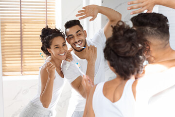 Fototapeta premium Morning Hygiene. Joyful Middle Eastern Couple Brushing Teeth And Dancing In Bathroom