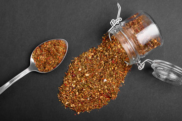 A mixture of various spices in a spoon and poured out of a jar on a black background.