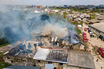 Fototapeta na wymiar Aerial view of firefighters extinguishing ruined building on fire with collapsed roof and rising dark smoke