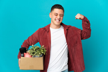 Young caucasian man making a move while picking up a box full of things isolated on blue background...