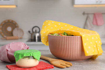 Bowl of fresh salad covered with beeswax food wrap on light grey table in kitchen - obrazy, fototapety, plakaty