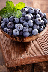 Bowl of fresh blueberries on rustic wooden board. Organic food blueberries and mint leaf for healthy lifestyle.