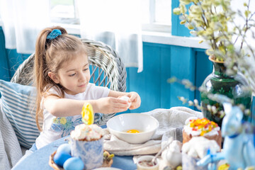 Obraz na płótnie Canvas pretty little Armenian girl helps with baking for Easter on veranda on sunny spring day decorated with flowers and Easter decor, eggs, cake and willow branches, Easter family celebration