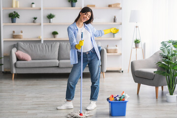 Portrait of excited woman cleaning floor singing holding mop