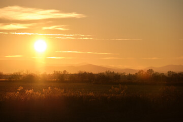 Beautiful evening panoramic landscape with bright setting sun over distant mountain peaks and asphalt road in front at sunset