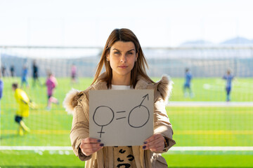 Close-up of a young Caucasian woman holds a poster board with a symbol of gender equality drawn on...
