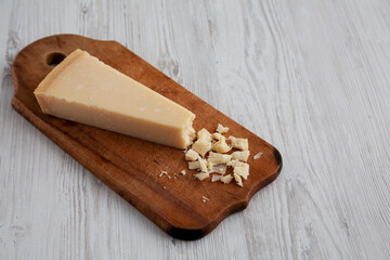 A Piece of Parmigiano Reggiano on a rustic wooden board on a white wooden table, side view. Copy space.