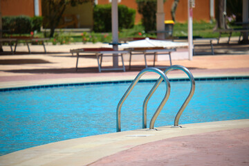 Close up of swimming pool stainless steel handrail descending into tortoise clear pool water. Accessibility of recreational activities concept