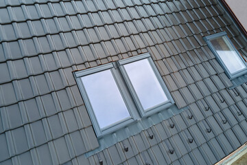 Closeup of attic window on house roof top covered with ceramic shingles. Tiled covering of building