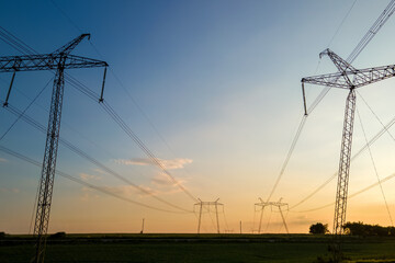 Dark silhouette of high voltage towers with electric power lines at sunrise