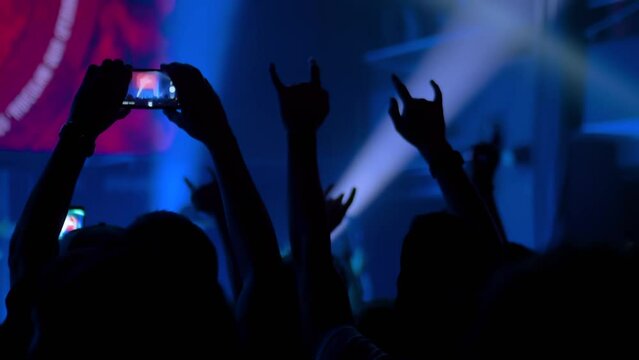 Slow motion: people hands silhouette taking photo or recording video of live music concert with smartphone. Crowd partying in front of stage. Photography, entertainment, technology concept