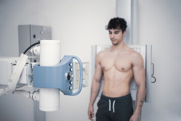 In the hospital, a man is leaning against an x-ray machine. Look for fractures, broken limbs, breast, cancer, or tumor. modern hospital.