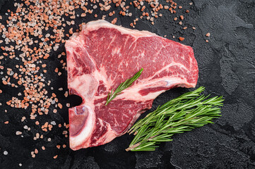 Raw T bone beef meat steak, porterhouse steak on butcher table with rosemary. Black background. Top...