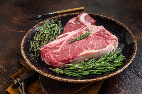 Dry Aged Raw Porterhouse Beef Meat Steak, Fresh T Bone On Rustic Plate With Spices. Dark Background. Top View