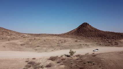 Car driving on gravel road in aerial desert. Sandy landscape, nobody in Namibia.
