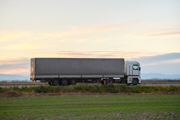 Semi-truck with cargo trailer driving on highway hauling goods in evening. Delivery transportation and logistics concept