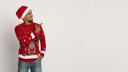 Handsome black man in Santa hat pointing at copy space