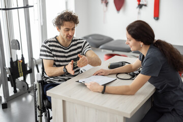 Medical worker talking with a young man in a wheelchair before training in the rehabilitation...