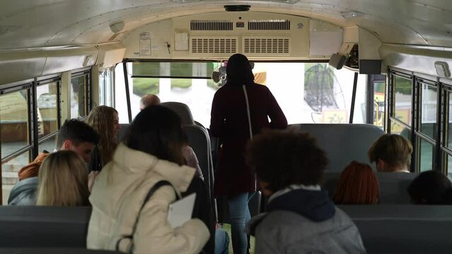 Multiracial secondary school pupils getting up and walking to exit from school bus. Multinational high school students sitting on their seats and getting off school bus upon arriving at class