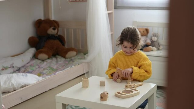Funny little girl in a yellow sweater enjoys playing with wooden pieces. Non-toxic toys for child development.