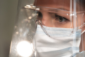 Young woman doctor or nurse working. Girl in medical mask, glasses and shield.