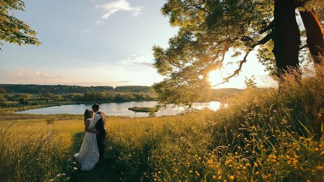 A happy young couple spends an hour at the lake at sundown. The warm sunset of the sun and the edge of the nature of that lake. The woman in arms closed her eyes and enjoys the receiving moments of