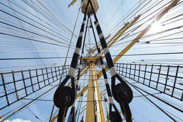 a view from below of the huge mast of an old sailing ship, many ropes hanging down from above, blue...