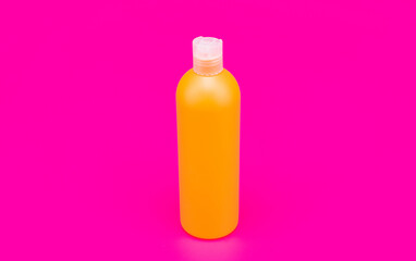 orange shampoo bottle on pink background, hygiene