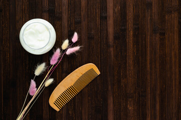 Ecological cosmetics. An open jar with a hair mask, a natural wood comb and dry flowers on a dark...