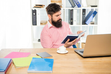Serious professional man reading book at office desk