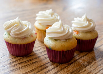Four mini spring cupcakes on a rough wooden table.  White frosting with no sprinkles.