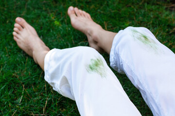 Barefoot girl sitting dirty stain of grass on white pants on a background of green field. top view....