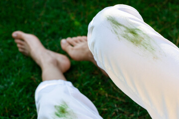 Barefoot girl sitting dirty stain of grass on white pants on a background of green field. top view....