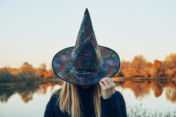 A girl in a black coat, holding the witch's hat on her head with her hand. Lake, autumn, dry...