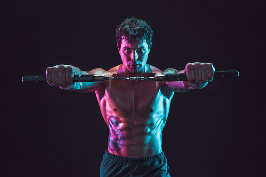 Portrait of muscular man who holds nunchaku while isolated on black background. Sport concept