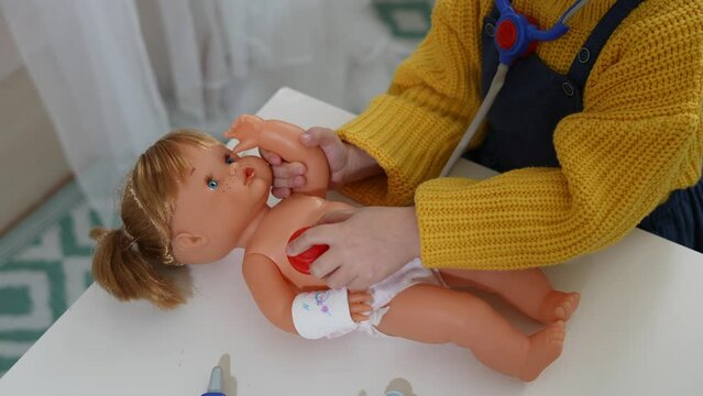 Little girl playing doctor with her toys. Children's hands putting a toy phonendoscope on their doll to do a check-up.
