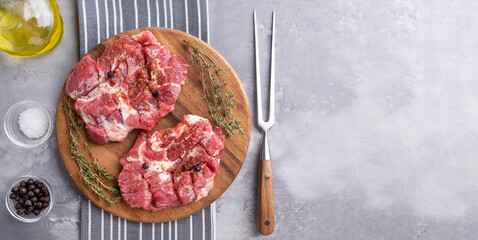 Raw pork neck pieces with spices on a wooden board. Top view, space for text