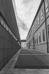a narrow concrete road among the high facades of industrial buildings on the sides against a cloudy sky. Black and white photography