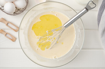 Cooking dough for traditional thin pancakes or crepes. Eggs, flour, salt, sugar, milk and butter in a bowl on a white wooden background. Recipe step by step. Food for Maslenitsa.
