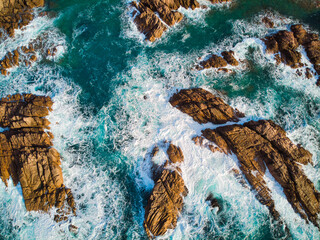aerial bird's eye drone view of rocks that emerge in the turquoise sea with the foamy waves breaking, An aerial view of the beautiful Mediterranean sea, where you can se the rocky textured underwater 