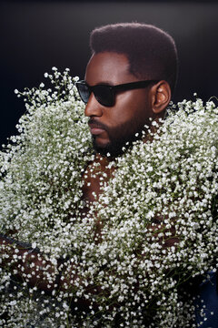 Black bearded attractive man in sunglasses wearing white gypsaphylla flowers.