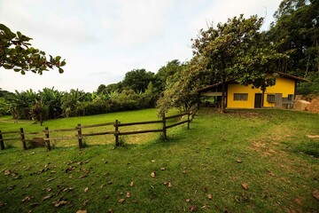 Casa amarela de fazenda em meio a um campo verde com cerca de madeira. 