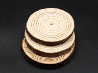 Three round planks of wood with bark and pronounced rings, arranged one on top of the other, on a black background.