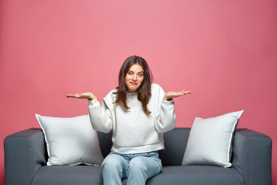 Puzzled young girl shrugging shoulders, dont know answer, sitting on sofa. Dilemma, uncertainty concept
