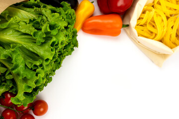 Fresh colorful organic vegetables and a bag of dry pasta on a white background, the concept of cooking an Italian dish. Copy space. flat lay