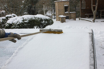 A man clears snow from an outdoor pool in a private yard. Water pool maintenance in winter.