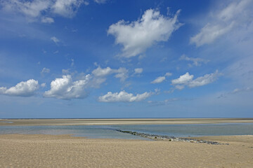 Kleine Brücke aus Steinen führt ins Wasser am Wattenmeer an der Nordsee bei blauem Himmel mit ein paar Wolken